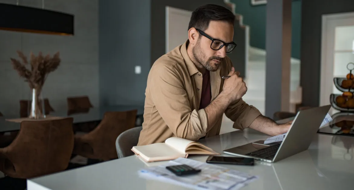 Young businessman working on laptop at home and paying bills and taxes.