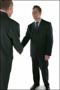 Two business men in suits shaking hands and smiling